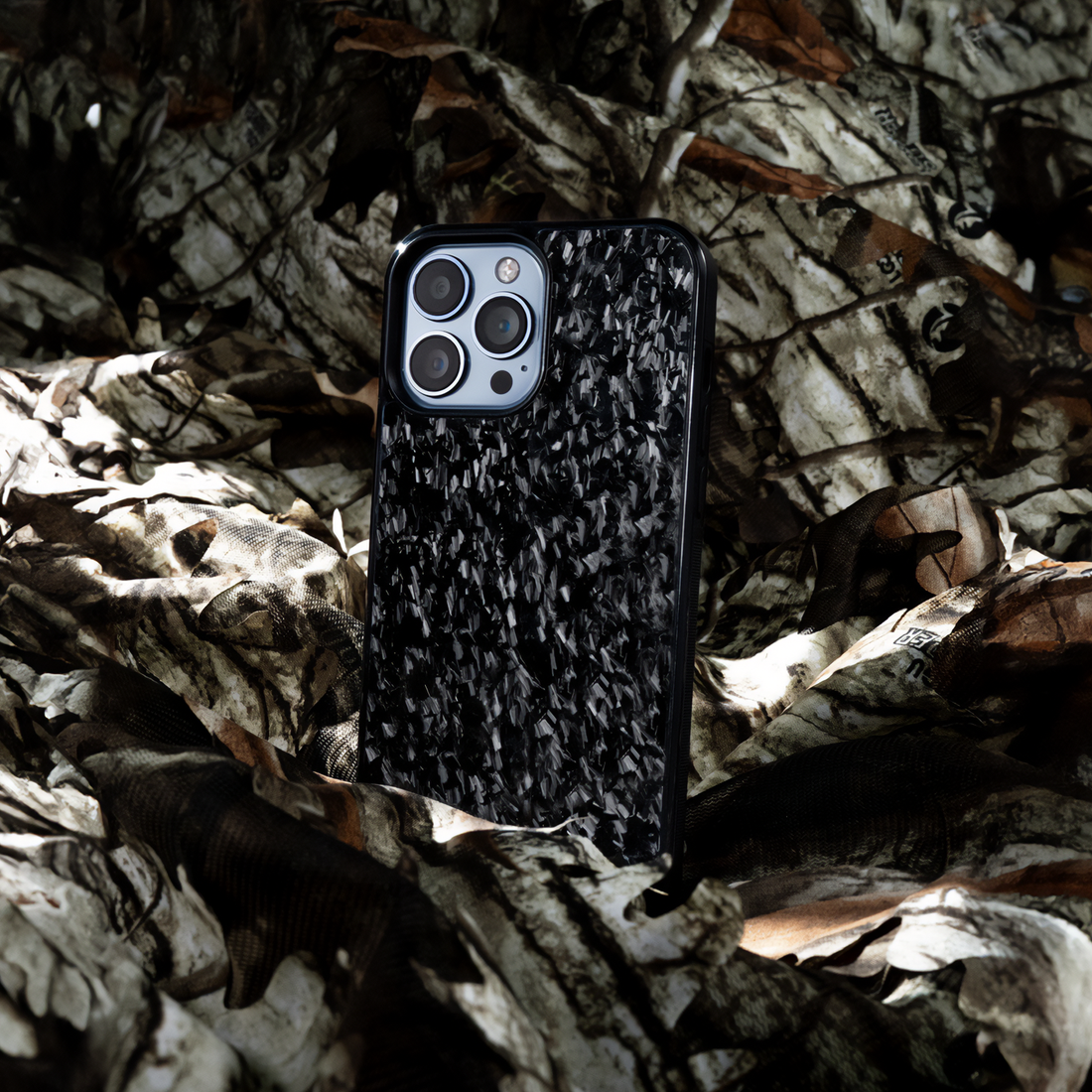 Forged black carbon fiber iPhone case standing in dry leaves, nature theme