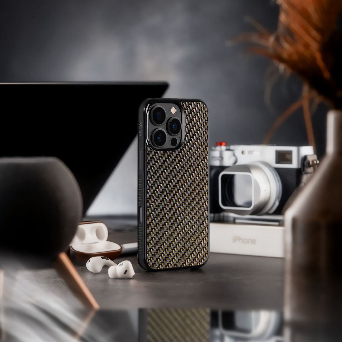 Gold carbon fiber iPhone case on desk, styled with camera and accessories