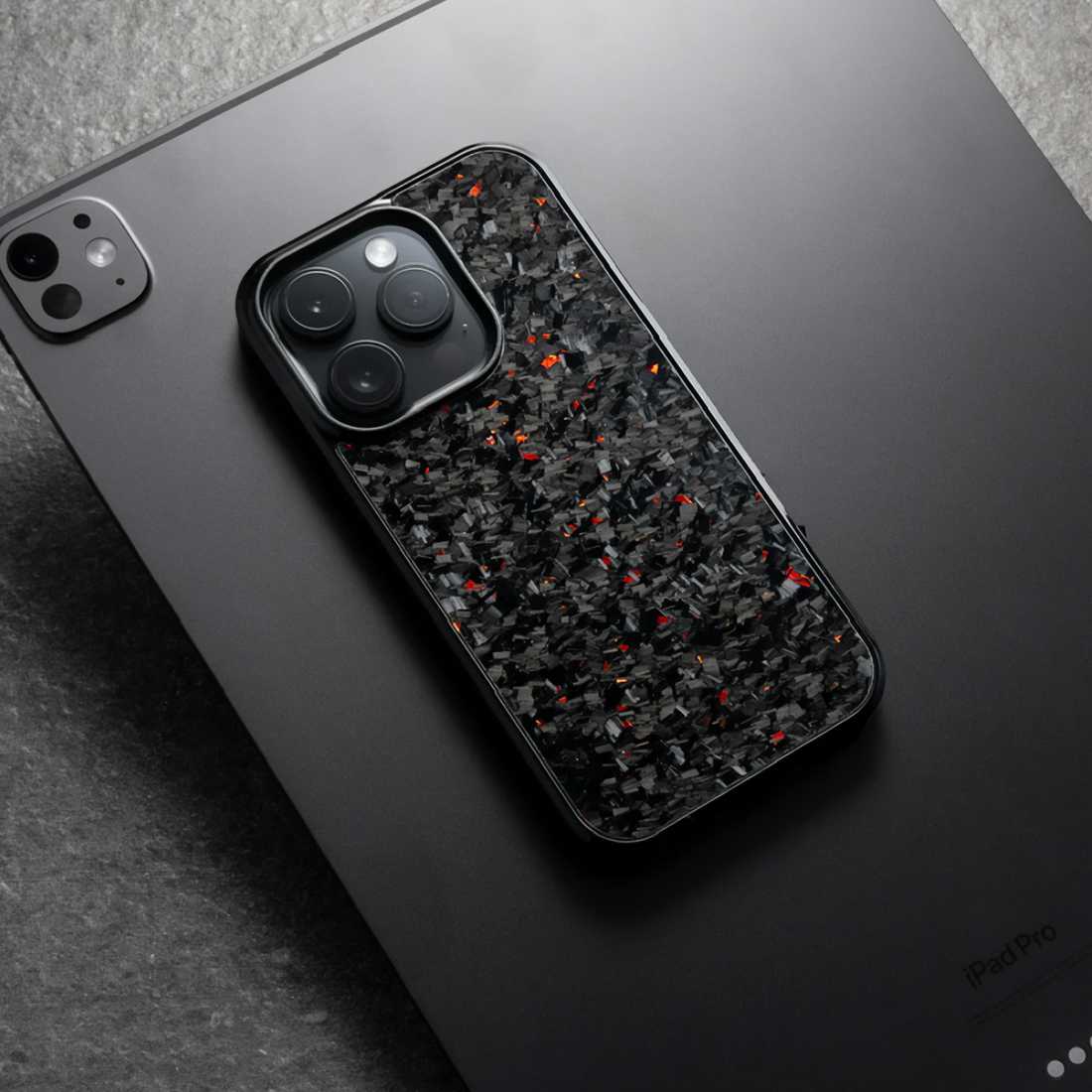 Red forged iPhone case placed on dark iPad surface, industrial theme